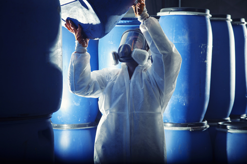 Man in hazmat suit and respirator lifting a blue barrel